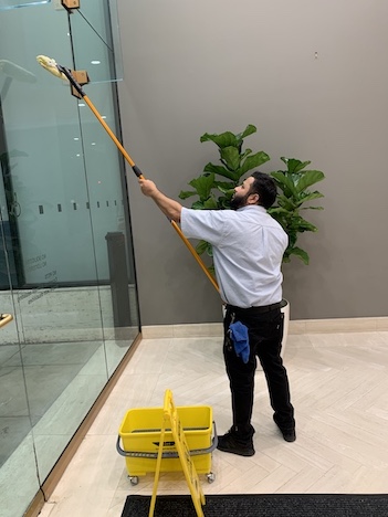 custodial and grounds worker cleaning a glass window